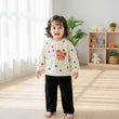 Children's outfit with polka dot shirt featuring cartoon characters and black pants on a white surface.